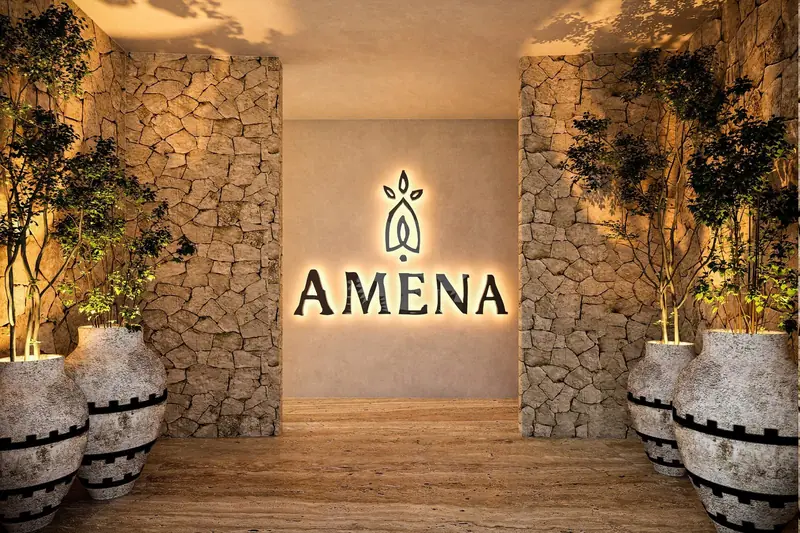 Acceso con muros de piedra y el logotipo de Amena iluminado